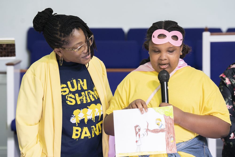 A Sunshine Band mentor helping a child share at the microphone