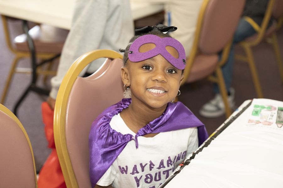 A young girl in a purple superhero mask and cape