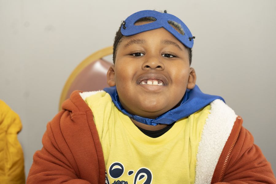 A young boy in a blue superhero mask smiling big